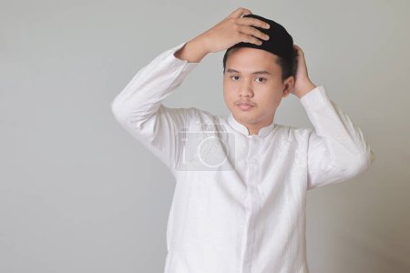 Portrait of Asian muslim man trying to wear songkok or black skullcap. Isolated image on white background