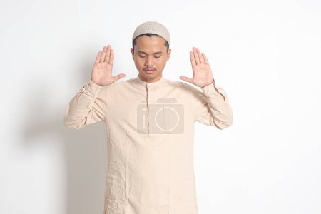 Porträt eines religiösen asiatischen muslimischen Mannes im Kokohemd mit Totenkopf, der mit erhobenen Händen betet und vor dem Gebet takbir sholat macht. Isoliertes Bild auf weißem Hintergrund