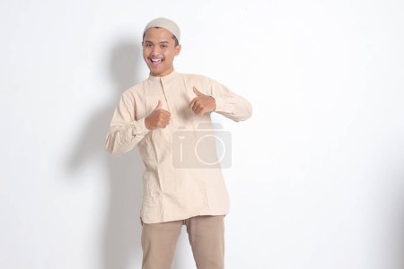 Portrait of attractive Asian muslim man in koko shirt showing thumb up, good job hand gesture. Approval concept. Isolated image on white background