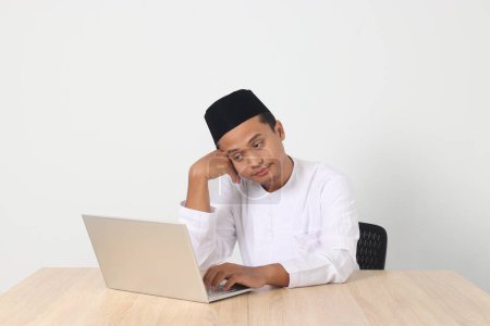 Téléchargez les photos : Portrait d'homme musulman asiatique fatigué en chemise koko avec calotte crânienne travaillant pendant le jeûne du mois de ramadan, somnolent, bâillant avec la main couvrant la bouche. Image isolée sur fond blanc - en image libre de droit