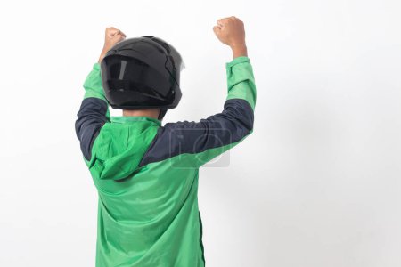 Téléchargez les photos : Vue arrière du chauffeur de messagerie en ligne asiatique portant une veste verte et un casque levant le poing, célébrant le succès. Image isolée sur fond blanc - en image libre de droit