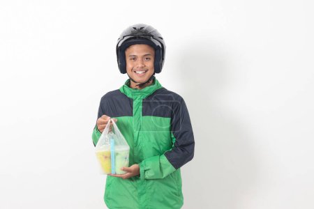 Téléchargez les photos : Portrait de chauffeur de taxi en ligne asiatique portant une veste verte et un casque livrant les boissons dans une tasse en plastique au client. Image isolée sur fond blanc - en image libre de droit