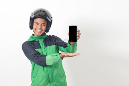 Téléchargez les photos : Portrait d'un chauffeur de taxi asiatique en ligne portant une veste verte et un casque montrant et présentant un téléphone portable à écran blanc. Image isolée sur fond blanc - en image libre de droit