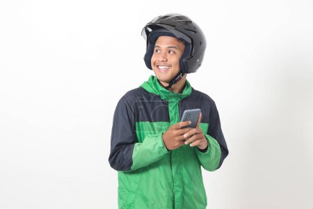 Téléchargez les photos : Portrait de chauffeur de taxi en ligne asiatique portant une veste verte et un casque tenant un téléphone portable avec un visage d'expression souriant. Image isolée sur fond blanc - en image libre de droit