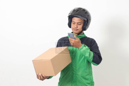 Téléchargez les photos : Portrait d'un chauffeur de taxi asiatique en ligne portant une veste verte et un casque tenant une boîte et scannant ou capturant le colis. Image isolée sur fond blanc - en image libre de droit