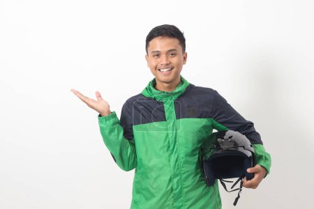 Téléchargez les photos : Portrait de chauffeur de taxi en ligne asiatique portant vert debout sur fond blanc, souriant et regardant la caméra, tenant son casque sur le côté - en image libre de droit