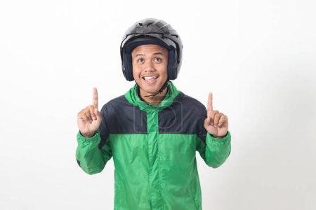 Téléchargez les photos : Portrait de chauffeur de taxi en ligne asiatique portant une veste verte et un casque pointant vers l'espace vide avec le doigt. Image isolée sur fond blanc - en image libre de droit