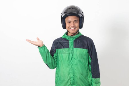 Téléchargez les photos : Portrait de chauffeur de taxi en ligne asiatique portant une veste verte et un casque pointant vers l'espace vide avec le doigt. Image isolée sur fond blanc - en image libre de droit