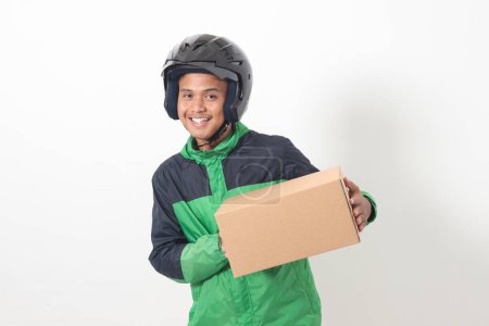 Téléchargez les photos : Portrait de chauffeur de messagerie en ligne asiatique portant veste verte et casque livraison paquet et boîte pour le client. Image isolée sur fond blanc - en image libre de droit