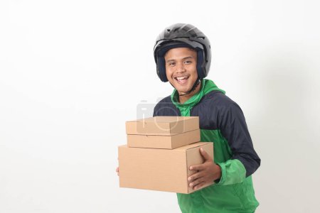 Téléchargez les photos : Portrait de chauffeur de messagerie en ligne asiatique portant veste verte et casque livraison paquet et boîte pour le client. Image isolée sur fond blanc - en image libre de droit