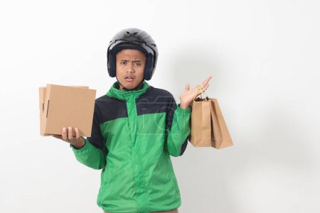 Téléchargez les photos : Portrait de chauffeur de messagerie en ligne asiatique portant une veste verte et un casque donnant sac à provisions en papier artisanal et paquet boîte. Image isolée sur fond blanc - en image libre de droit