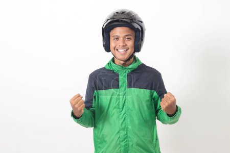 Téléchargez les photos : Portrait de chauffeur de taxi en ligne asiatique portant une veste verte et un casque levant le poing, célébrant le succès. Image isolée sur fond blanc - en image libre de droit