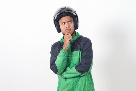 Téléchargez les photos : Portrait de chauffeur de taxi en ligne asiatique portant une veste verte et un casque réfléchissant à la question avec la main sur le menton. Image isolée sur fond blanc - en image libre de droit