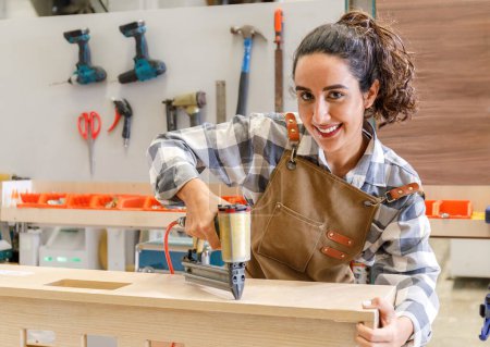 Téléchargez les photos : Portrait Jeune femme latine charpentier utilisant clou tir sur bois. restaurer le mobilier dans l'atelier de menuiserie Concept de jeunes start-up et concept de PME - en image libre de droit