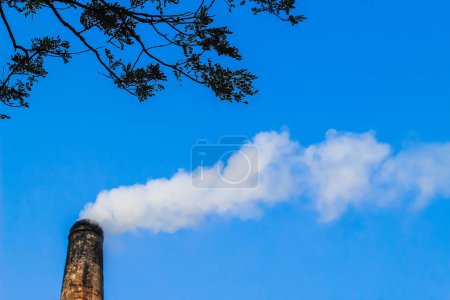 Der Schornstein des Ziegelfeldes emittiert starken Rauch mit ungesundem Kohlendioxid, das für die Schädigung der Ozonschicht verantwortlich ist. Fabrikrauch verursacht Luftverschmutzung. Qualmender Schornstein gegen blauen Himmel.