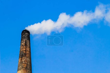 Der Schornstein des Ziegelfeldes emittiert starken Rauch mit ungesundem Kohlendioxid, das für die Schädigung der Ozonschicht verantwortlich ist. Fabrikrauch verursacht Luftverschmutzung. Qualmender Schornstein gegen blauen Himmel.
