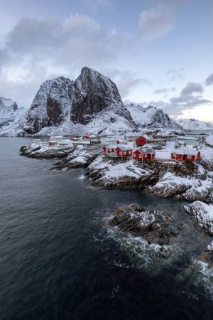 Foto de Una casa roja en una costa rocosa con una montaña en el fondo - Imagen libre de derechos