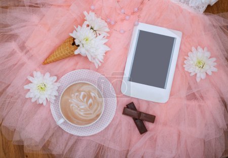 Romantic flat lay composition with cup of coffee,  e-book reader with copy space, white lowers and chocolate on lightweight fabric mesh lace. Template for feminine blog social media.