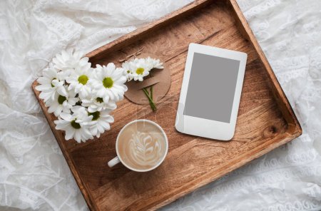 Composición romántica con taza de café, flores blancas y lector electrónico con espacio para copiar en bandeja de madera. Plantilla para blog femenino redes sociales.