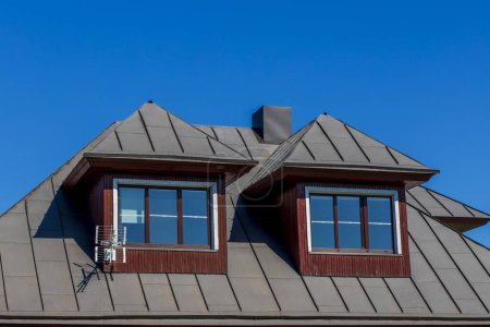 Haus Dachboden Nahaufnahme blauer Himmel Hintergrund. Fenster am Reihenhaus und Dachschindel auf blauem Himmelshintergrund.