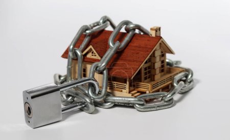 The house against the white background is bound by chains and closed locks. Housing security and building protection with locks.