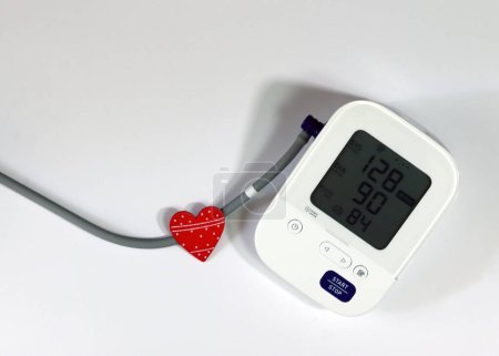 Rotes Herz und Blutdruckmessgerät zur Diagnose von Herzkrankheiten. Digitales Blutdruckmessgerät und Herz auf weißem Hintergrund.