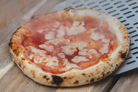 Téléchargez les photos : Servant une pizza chaude Margherita avec sauce tomate et mozzarella avec une pelle sur une planche en bois, avec de la fumée - en image libre de droit