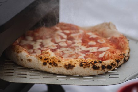 Téléchargez les photos : Cuisson ou cuisson de pizza chaude Margherita à la sauce tomate et mozzarella avec une pelle dans un four électrique ou à gaz, avec de la fumée, gros plan - en image libre de droit