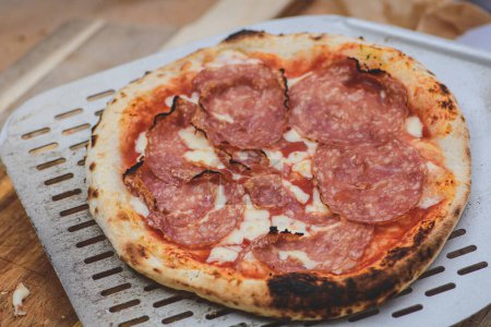 Téléchargez les photos : Servant une pizza chaude avec sauce tomate, mozzarella et salami avec une pelle sur une planche en bois, fermer - en image libre de droit