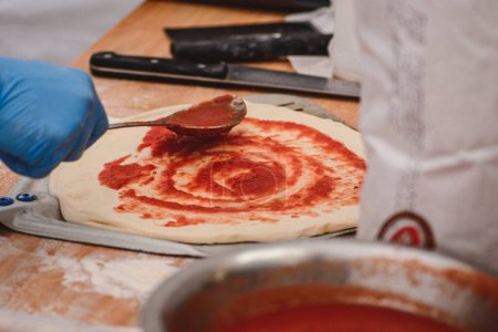 Téléchargez les photos : Ajouter la sauce tomate avec une cuillère sur la pâte à pizza sur une pelle sur une planche en bois, fermer - en image libre de droit