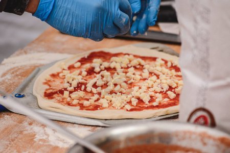 Téléchargez les photos : Main avec gant en plastique préparation de pizza avec sauce tomate et mozzarella fraîche sur une pelle sur une planche en bois, fermer - en image libre de droit