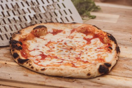 Téléchargez les photos : Servant une pizza chaude Margherita avec sauce tomate et mozzarella avec une pelle sur une planche en bois, avec de la fumée - en image libre de droit