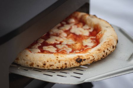 Téléchargez les photos : Cuisson ou cuisson de pizza chaude Margherita à la sauce tomate et fromage mozzarella avec une pelle dans un four électrique ou à gaz, avec de la fumée, gros plan - en image libre de droit