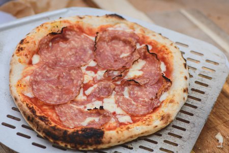 Téléchargez les photos : Servant une pizza chaude avec sauce tomate, mozzarella et salami avec une pelle sur une planche en bois, avec de la fumée - en image libre de droit