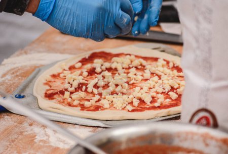 Téléchargez les photos : Main avec gant en plastique préparation de pizza avec sauce tomate et fromage mozzarella frais sur une pelle sur une planche en bois, fermer - en image libre de droit