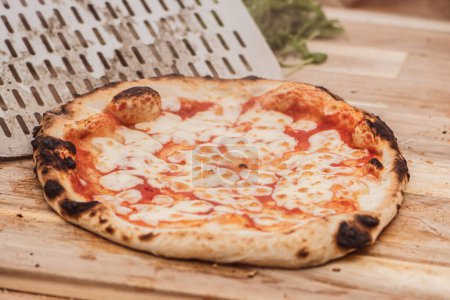 Foto de Sirve pizza caliente Margherita con salsa de tomate y queso mozzarella con una pala en una tabla de madera, con humo - Imagen libre de derechos