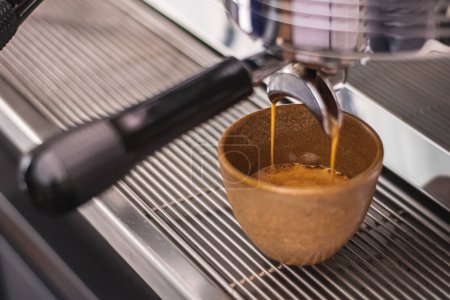 Téléchargez les photos : Preparing coffee with bar coffee machine, coffee is poured in a ceramic cup, close up - en image libre de droit