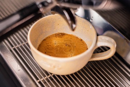 Téléchargez les photos : Preparing coffee with bar coffee machine, coffee is poured in a ceramic cup, close up - en image libre de droit