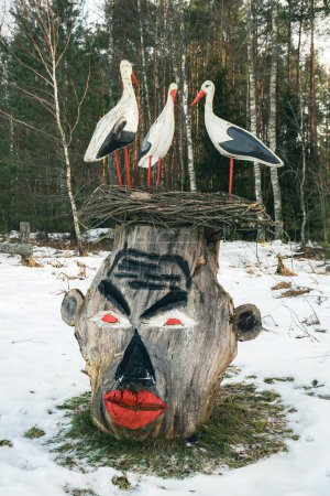 Photo for Wooden sculpture with three storks in the nest and indigenous mask carved in a trunk in the village of Margionys, Dzkija or Dainava region, Lithuania - Royalty Free Image