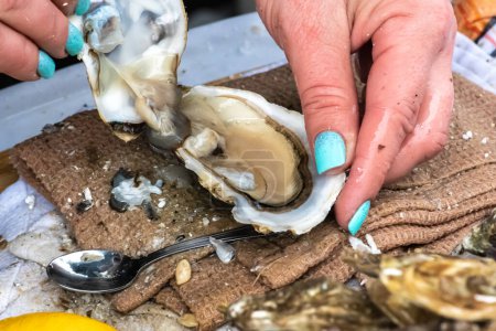 Photo for Wet hands of a girl with painted nails opening an oyster in a fish shop or street food market - Royalty Free Image