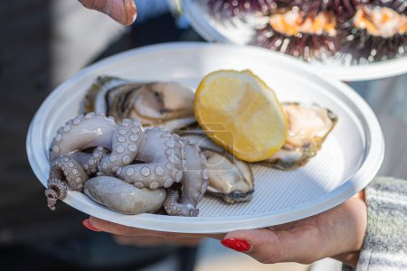Frische rohe Austern und Tintenfische zum Essen mit Zitrone in einem Teller auf einem Fischmarkt in Bari, Apulien, Italien