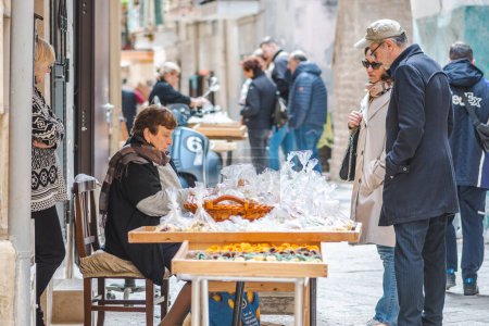 Téléchargez les photos : Bari, Italie - 5 avril 2023 : Femme âgée vendant aux touristes orecchiette fraîche ou orecchietta dans la vieille ville de Bari, faite avec du blé dur et de l'eau, pâtes artisanales typiques des Pouilles ou des Pouilles, Italie - en image libre de droit