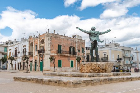 Téléchargez les photos : Polignano a Mare, Bari, Italie - 6 avril 2023 : Statue en bronze du chanteur italien Domenico Modugno face à la vieille ville sur les falaises rocheuses et la mer bleue à bras ouverts comme la célèbre chanson Volare - en image libre de droit
