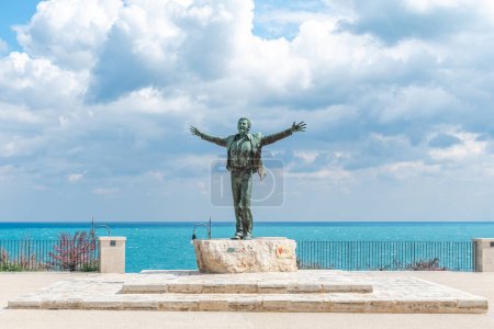 Photo for Polignano a Mare, Bari, Italy - April 6 2023: Bronze statue of the Italian singer Domenico Modugno facing the old town on the rocky cliffs and the blue sea with open arms as the famous song Volare - Royalty Free Image