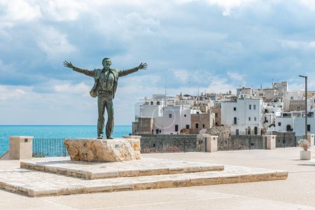 Téléchargez les photos : Polignano a Mare, Bari, Italie - 6 avril 2023 : Statue en bronze du chanteur italien Domenico Modugno face à la vieille ville sur les falaises rocheuses et la mer bleue à bras ouverts comme la célèbre chanson Volare - en image libre de droit