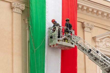 Téléchargez les photos : Bari, Pouilles, Italie - 5 juin 2023 : Pompiers déployant un grand drapeau italien sur un bâtiment historique avant une célébration ou un événement - en image libre de droit