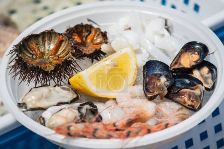Placa de fruta fresca cruda de mar o alimentos, lista para comer con erizos de mar, gambas, camarones, ostras, mejillones negros, sepia y limón en un mercado de pescado en Bari, Puglia, Italia