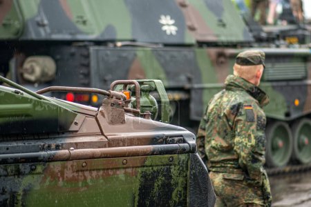 Photo for Berlin, Germany - June 17 2023: German soldier walking near moving armoured tanks self-propelled howitzer Panzerhaubitze 2000 or PzH 2000, German Army, Bundeswehr, NATO response force - Royalty Free Image
