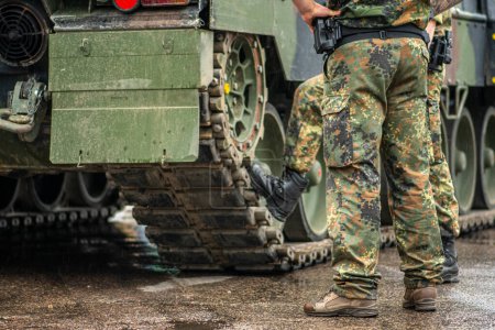 Téléchargez les photos : Deux soldats en uniforme de camouflage debout lors d'une pause sous la pluie près des traces d'un char blindé, seuls le pantalon et les bottes sont visibles - en image libre de droit