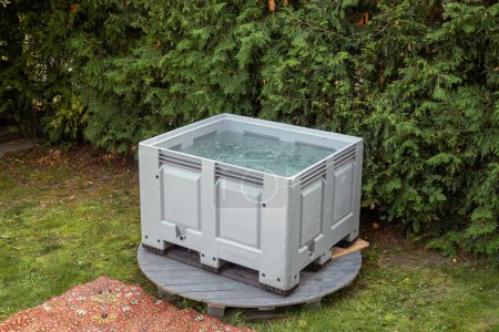 Portable plastic bath tub or tank in a garden ready for ice bathing in the cold water filled with ice cubes. Wim Hof Method, cold therapy, breathing techniques, yoga and meditation